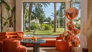Un salon moderne avec des meubles orange, une table basse en verre et une vue sur un jardin tropical.
