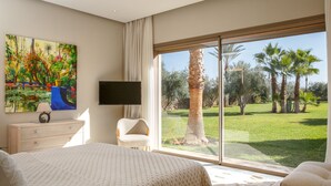 A bedroom with a large bed, a TV mounted on the wall, a chair, and a painting of a garden. - Villa Azkar - Three Bedroom Villa, Sleeps 6 (Marrakesh)