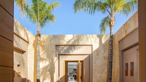 A modern building with a central open space, flanked by tall palm trees and stone walls. - Villa Azkar - Three Bedroom Villa, Sleeps 6 (Marrakesh)