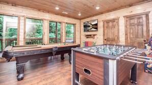 A wooden-floored room with a pool table, foosball table, and large windows. - Epic Stay: Private Pool, Theater & Games for 30 (Sevierville)