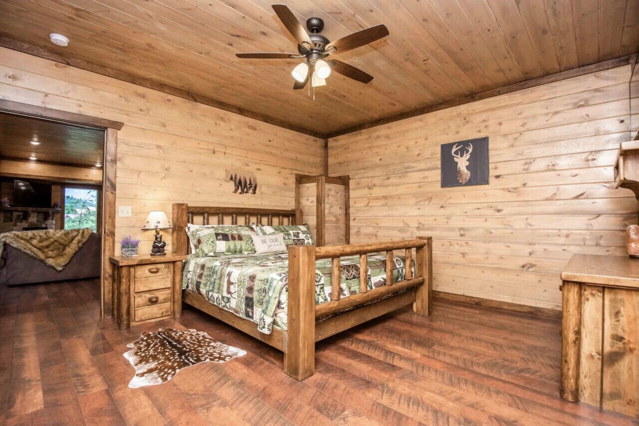 A wooden cabin bedroom with a bed, nightstands, a ceiling fan, and a deer rug.