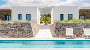 Un complexe hôtelier moderne doté d’une piscine, de murs en pierre et offrant une vue sur les montagnes.