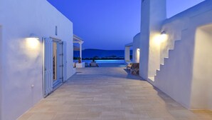 A corridor with a view of the sea at dusk, leading to a seating area with a pool. - Villa Irina - Five Bedroom Villa, Sleeps 10 (Makria Miti)