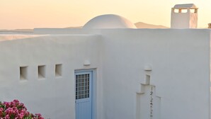 A white building with a blue door and small windows, set against a backdrop of mountains and a clear sky. - Villa Irina - Five Bedroom Villa, Sleeps 10 (Makria Miti)