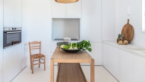 Una cocina moderna con armarios blancos, una mesa de comedor de madera, horno empotrado y una lámpara colgante.