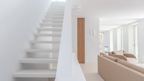Un interior moderno con una escalera, una puerta de madera y un sofá color beige.