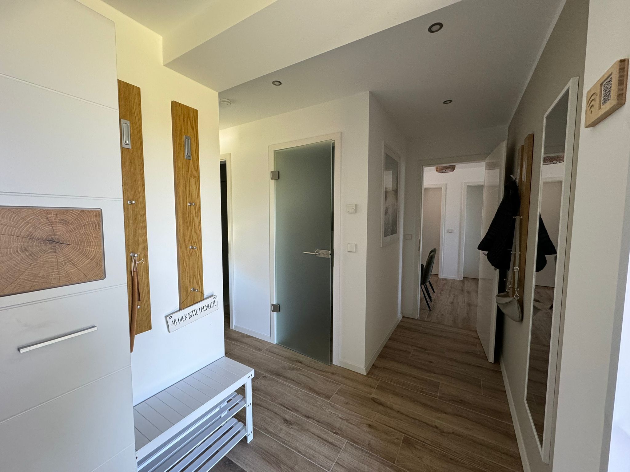 A modern hallway with wooden flooring, white walls, and a bench.