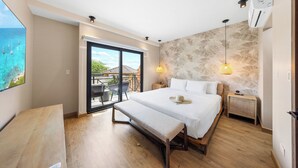 A bedroom with a bed, bench, bedside table, and a view of the ocean through a sliding door. - Bocobay Porta al Sole Condos (Noord)