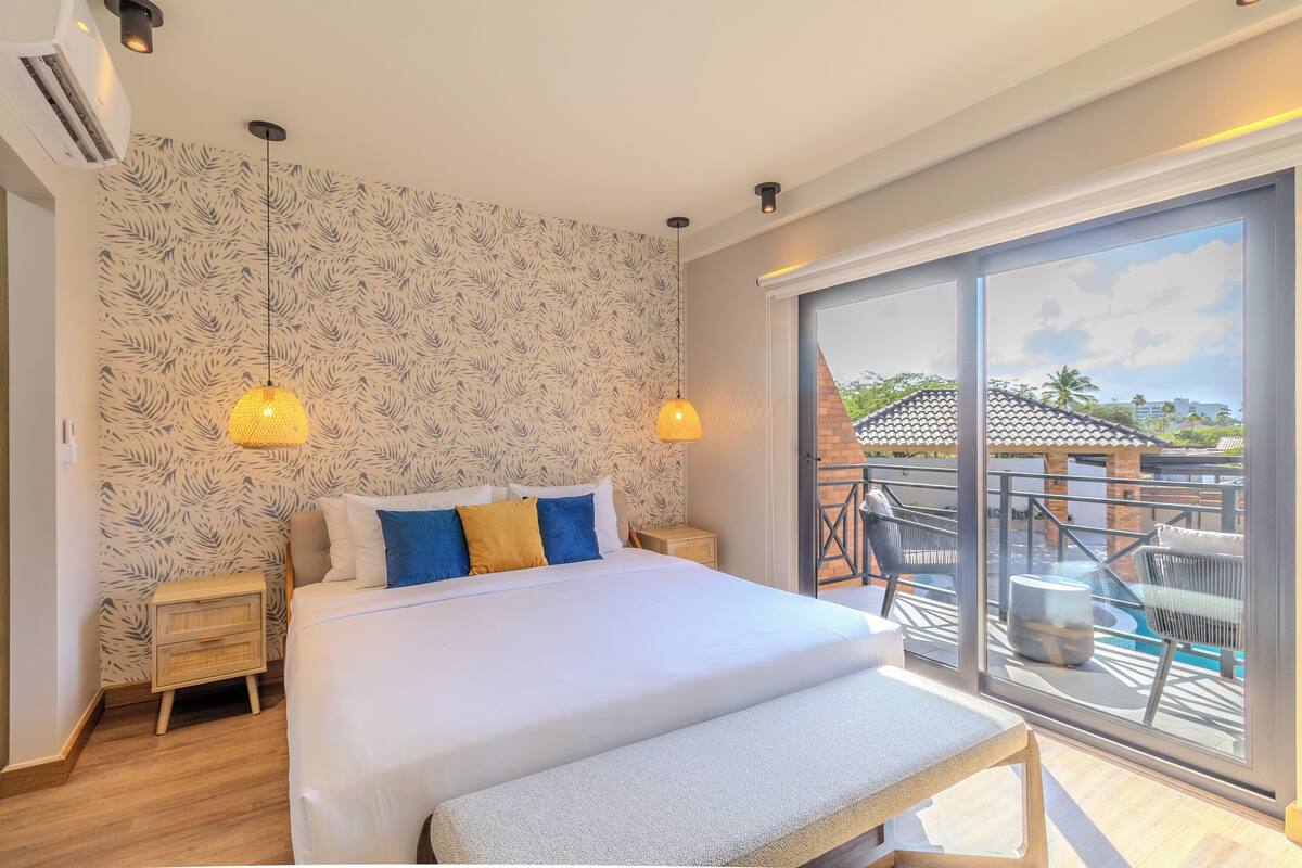 Un dormitorio con una cama grande, dos mesitas de noche, un banco, una ventana con vistas al exterior y un papel tapiz estampado.