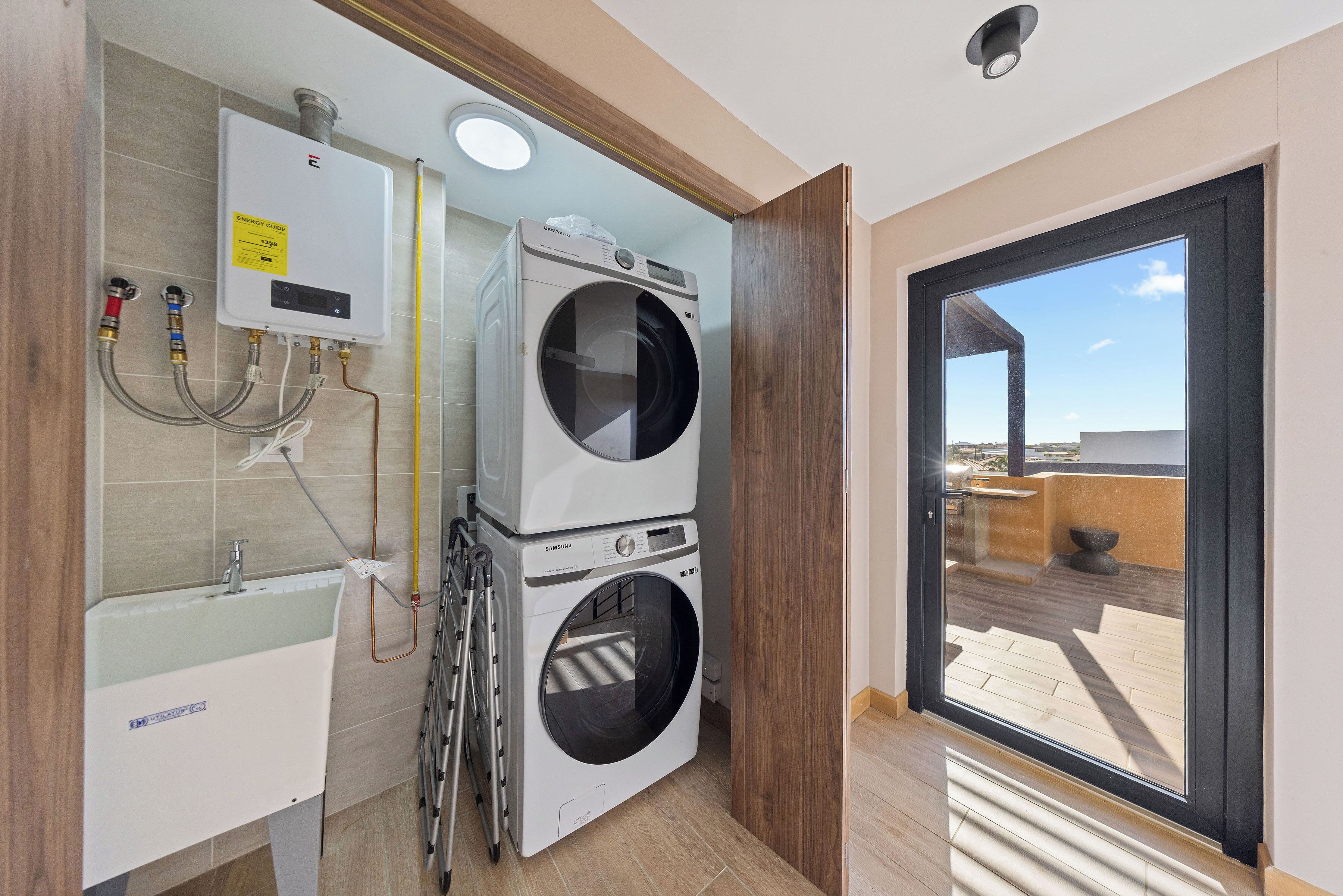 A compact laundry room with two stacked washing machines, a built-in sink, and a window providing a view of the outdoors.