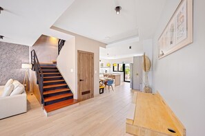 Un interior moderno con una escalera de madera, un comedor y una sala de estar con un sofá y una mesa de centro.
