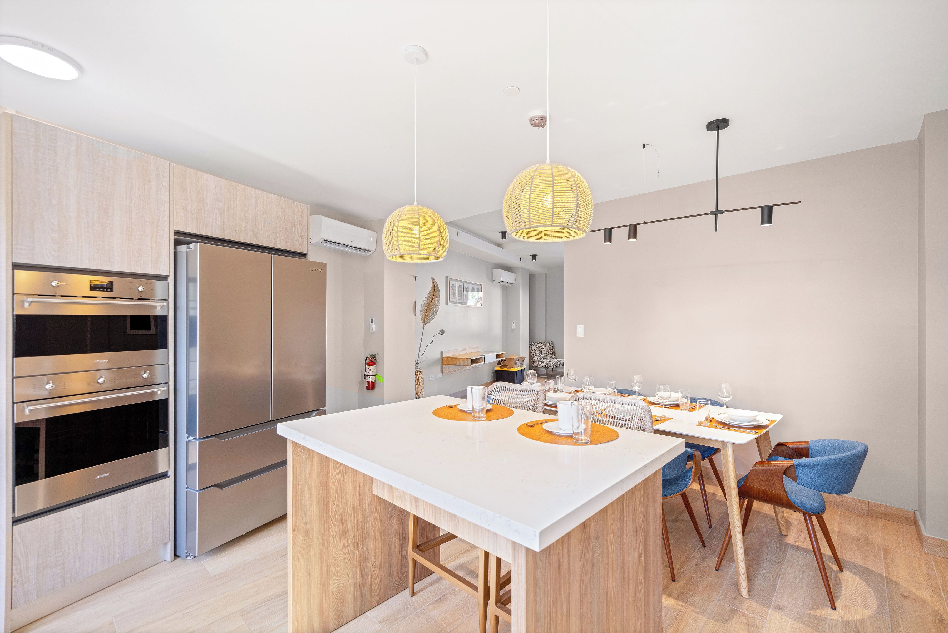 A modern kitchen with stainless steel appliances, a central island, and a dining area with blue chairs and a white table.