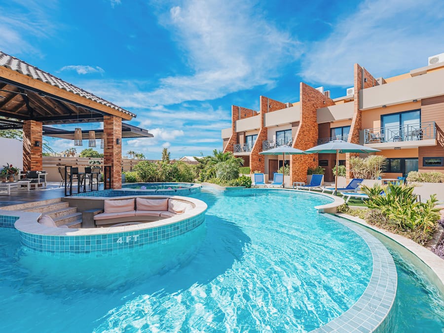 Una piscina con solárium, sillas de descanso y una zona de estar cubierta.