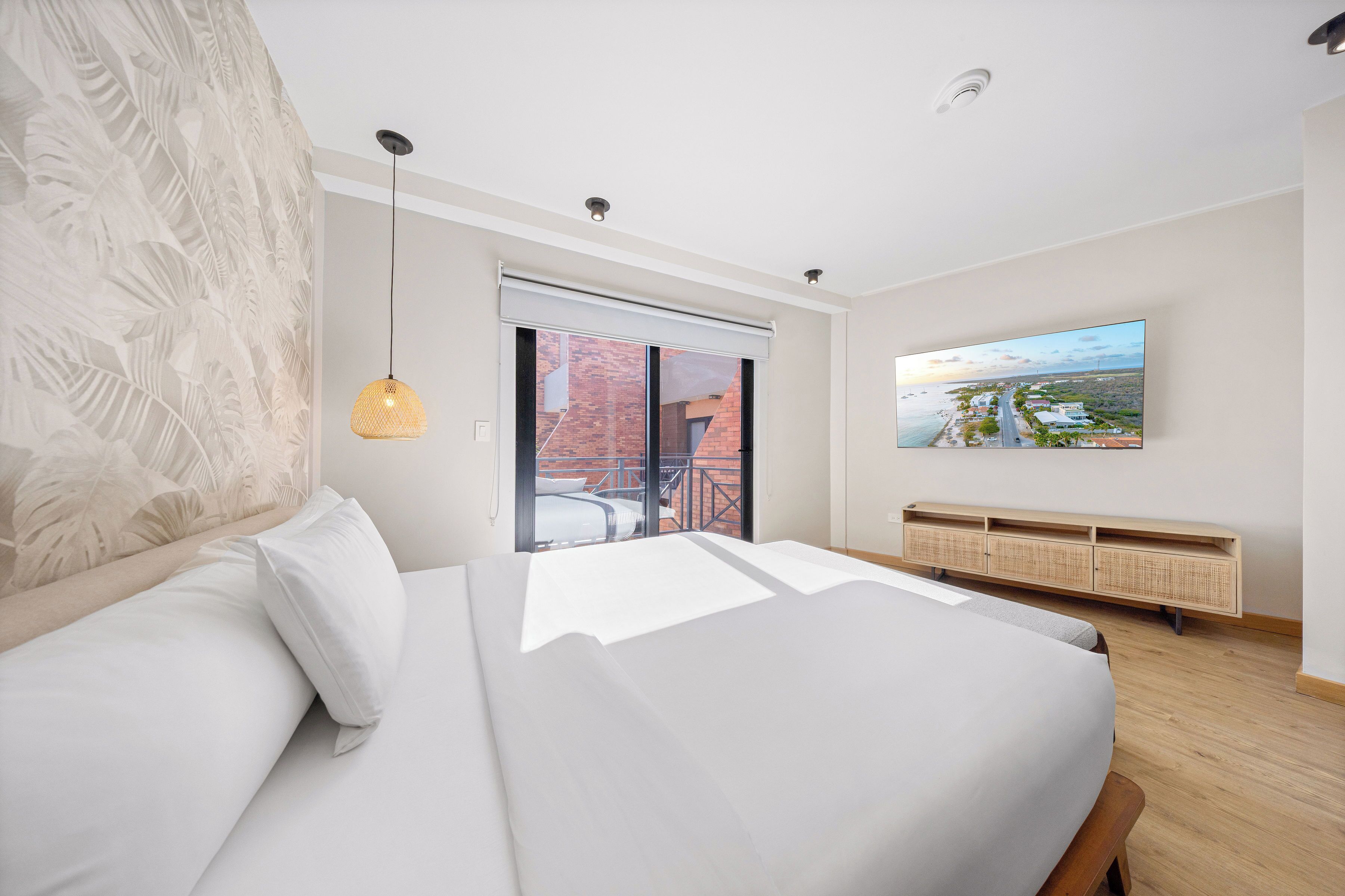 A modern bedroom with a large bed, a television, and a view of a brick building outside.