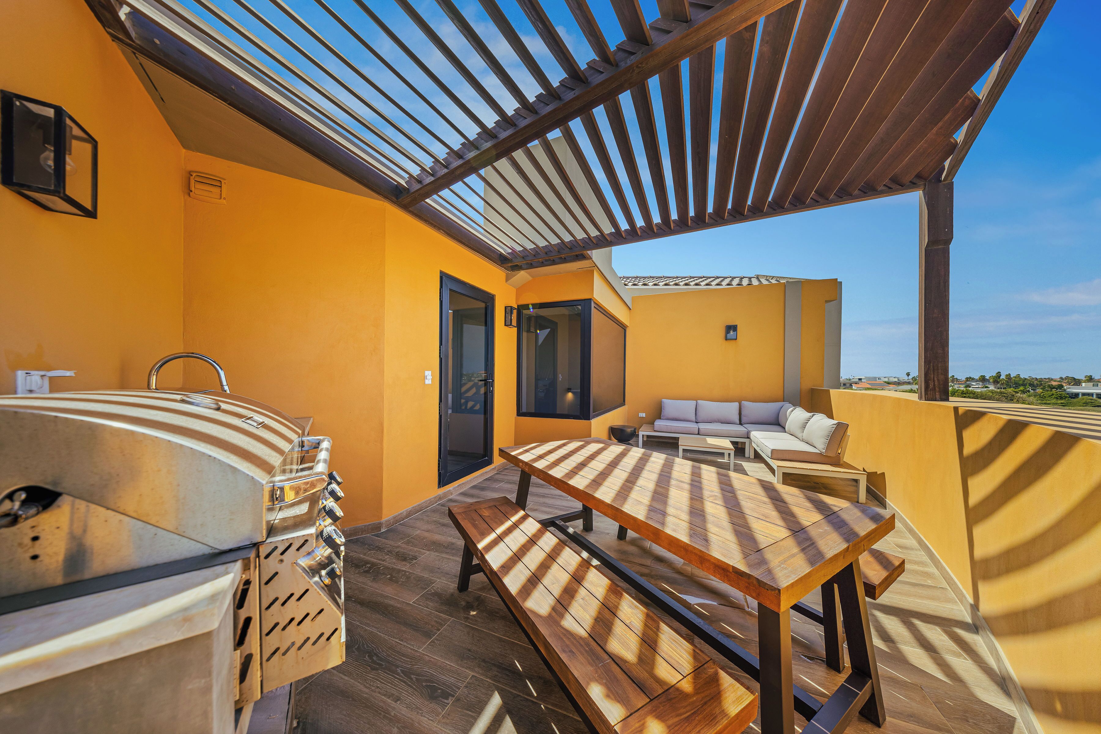 Un patio exterior con una parrilla, una mesa de madera y un sofá.