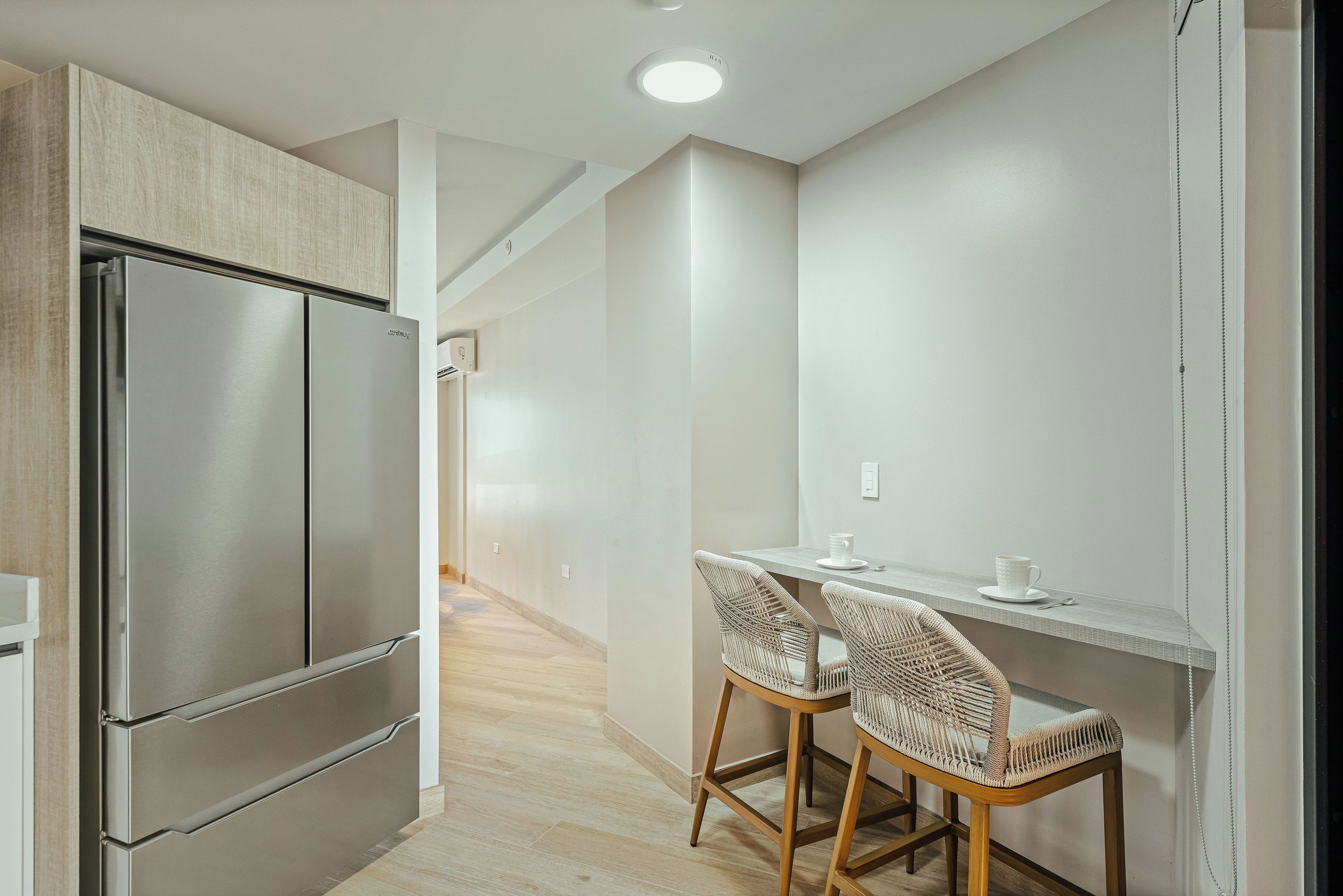 Una cocina moderna con un refrigerador de acero inoxidable, una mesa de comedor de madera y dos sillas de mimbre, además de una encimera blanca.