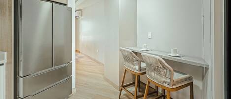 Una cocina moderna con un refrigerador de acero inoxidable, una mesa de comedor de madera y dos sillas de mimbre, además de una encimera blanca.