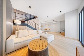 Una sala moderna con un sofá seccional, una mesa de centro redonda de madera y una escalera con barandilla negra.