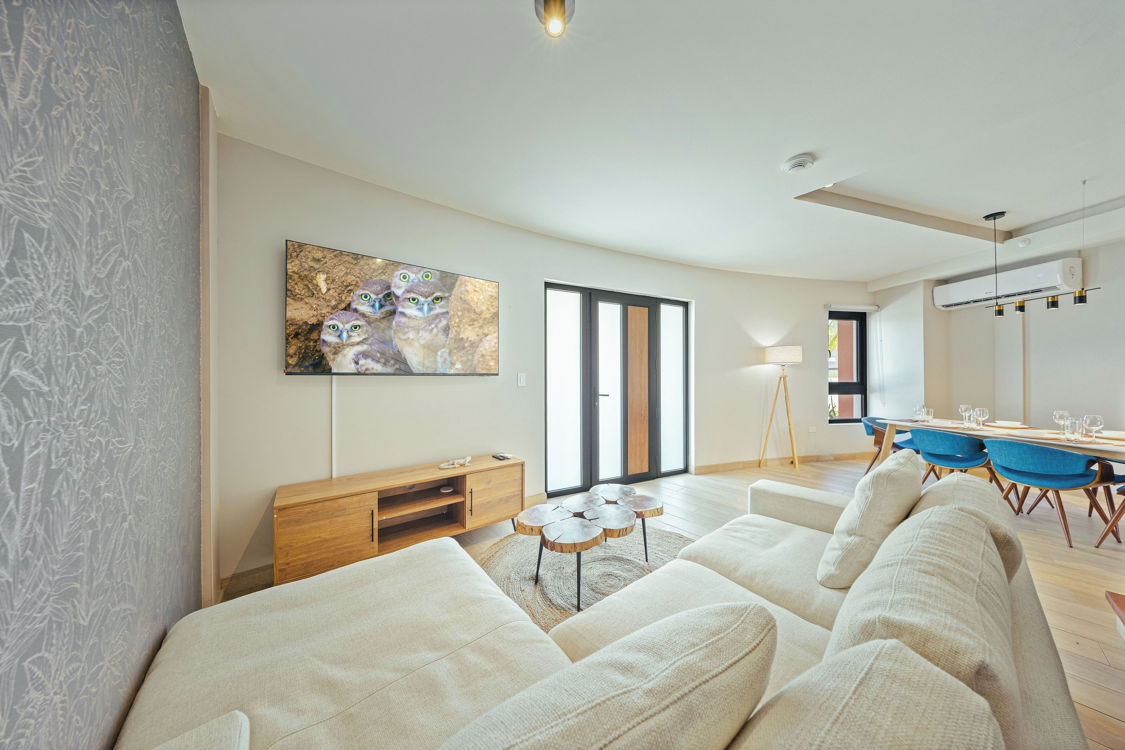 Un salon moderne avec un canapé, une table basse en bois, un tableau et un coin repas comprenant des chaises et une table.