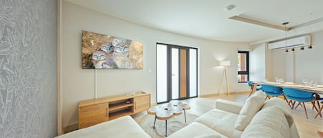 A modern living room with a sofa, a wooden coffee table, a painting, and a dining area with chairs and a table.