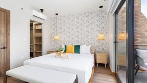 A bedroom with a large bed, bedside tables, a bench, an air conditioning unit, and a sliding glass door to a balcony. - Bocobay Porta al Sole Condos (Noord)