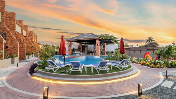 A pool area with lounge chairs and umbrellas, surrounded by a brick building and greenery. - Bocobay Porta al Sole Condos (Noord)