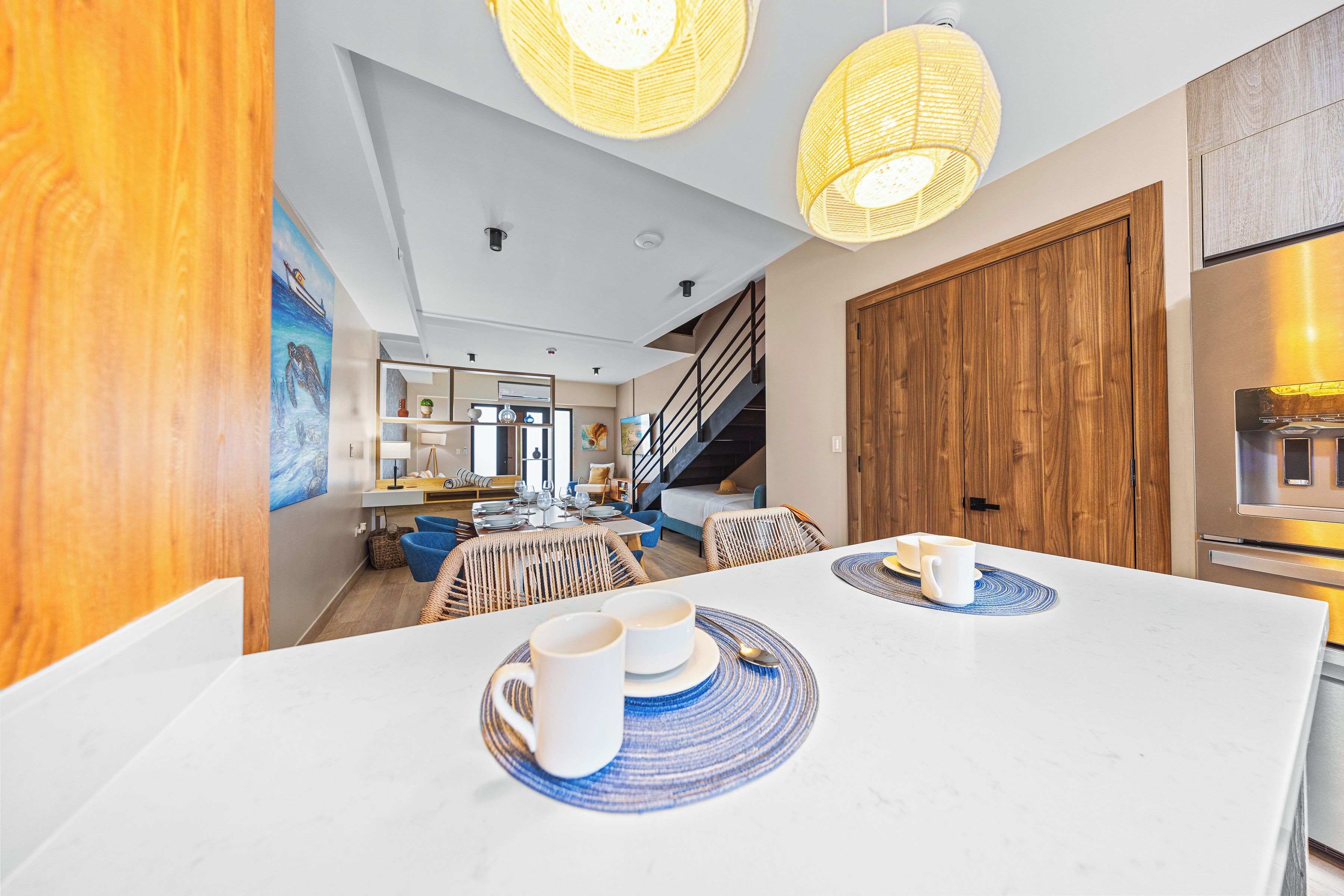 A modern kitchen with white countertops, a wooden door, and a stainless steel refrigerator.