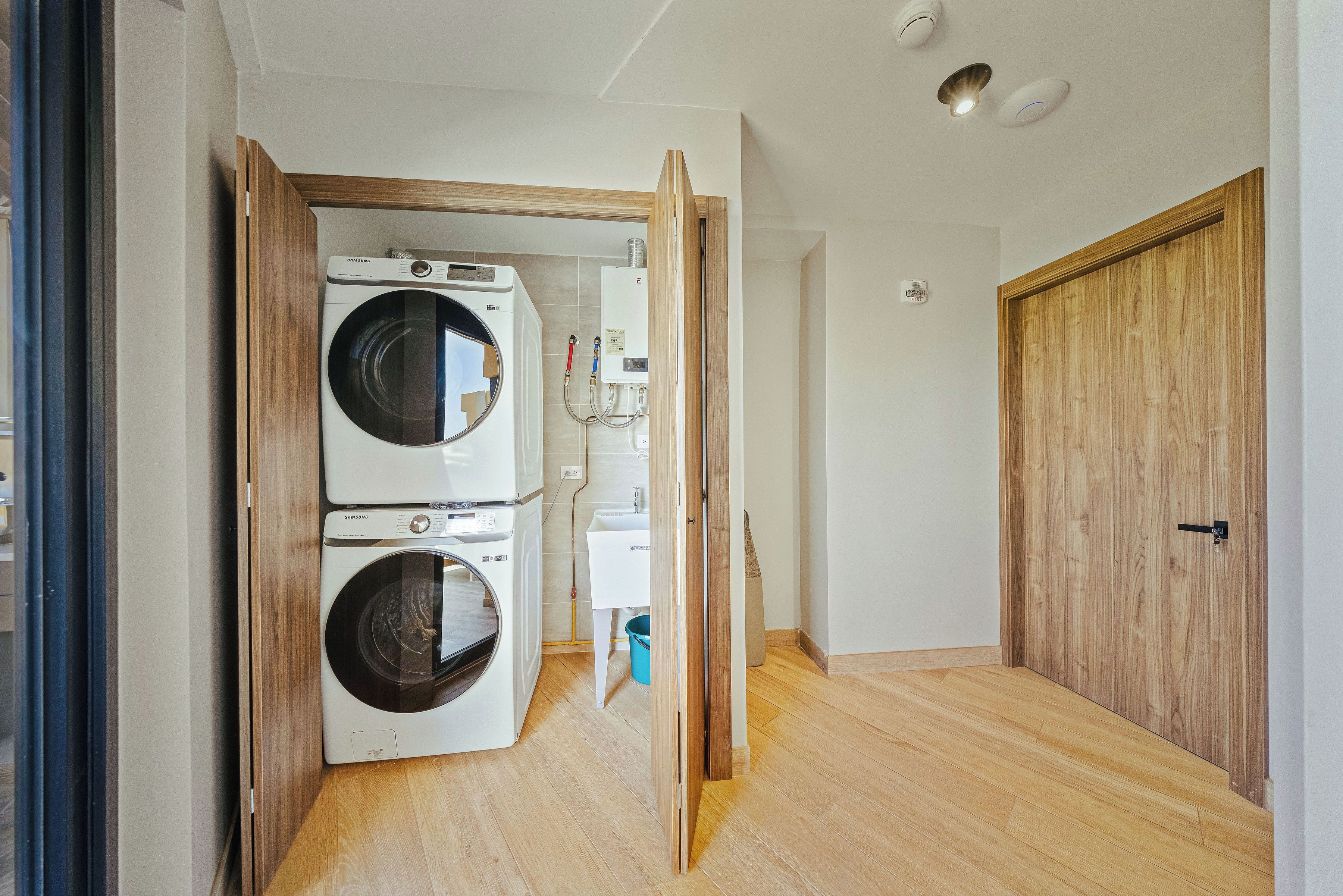 A laundry room with two stacked washing machines, a water heater, and a wooden door.