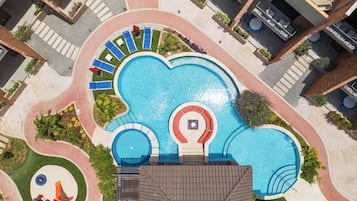 Vista aérea de un hotel con una gran piscina central, varias piscinas más pequeñas y una zona de juegos para niños.