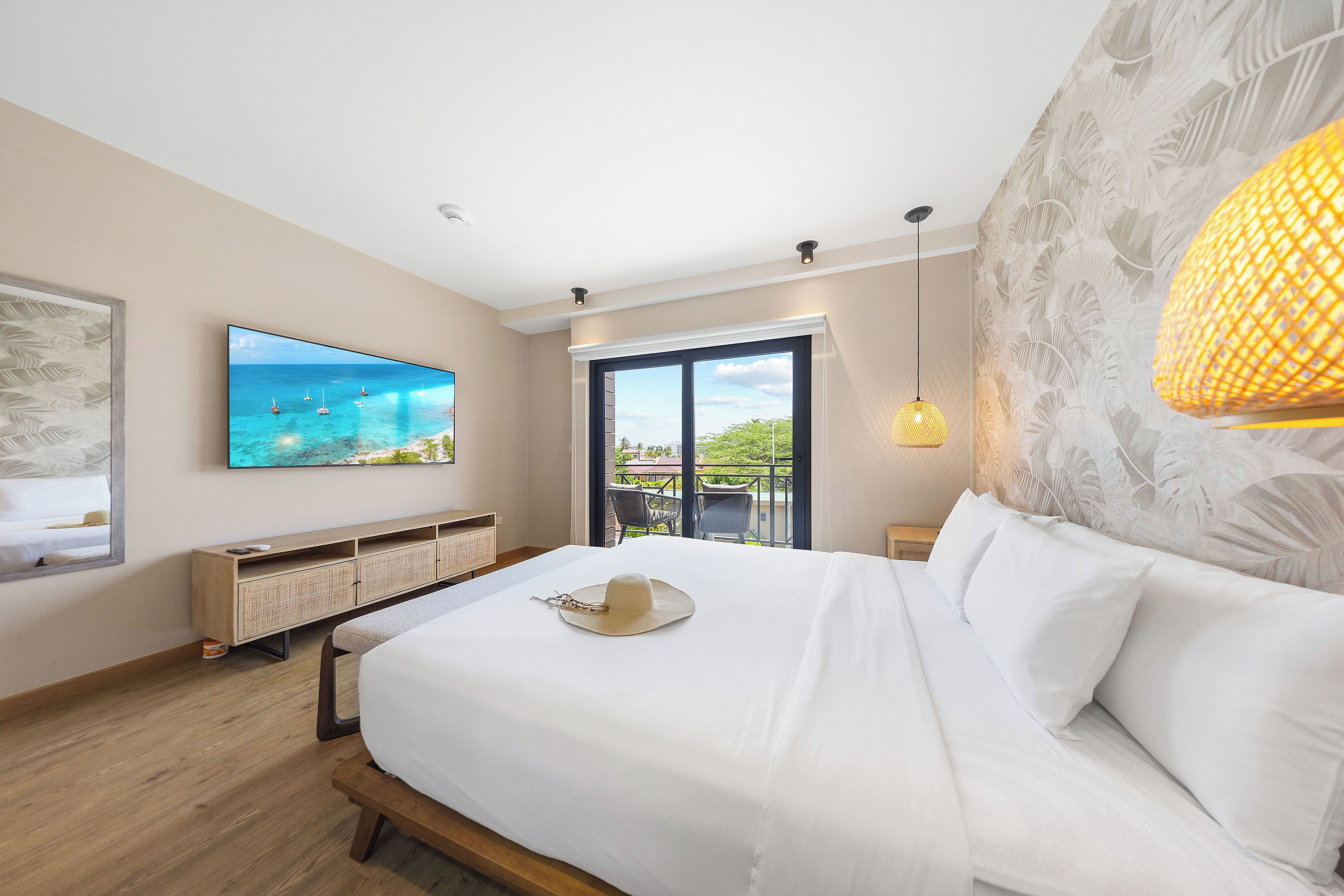 Habitación de hotel con una cama grande, un televisor montado en la pared, un balcón con vistas al mar y una lámpara de pared decorativa.