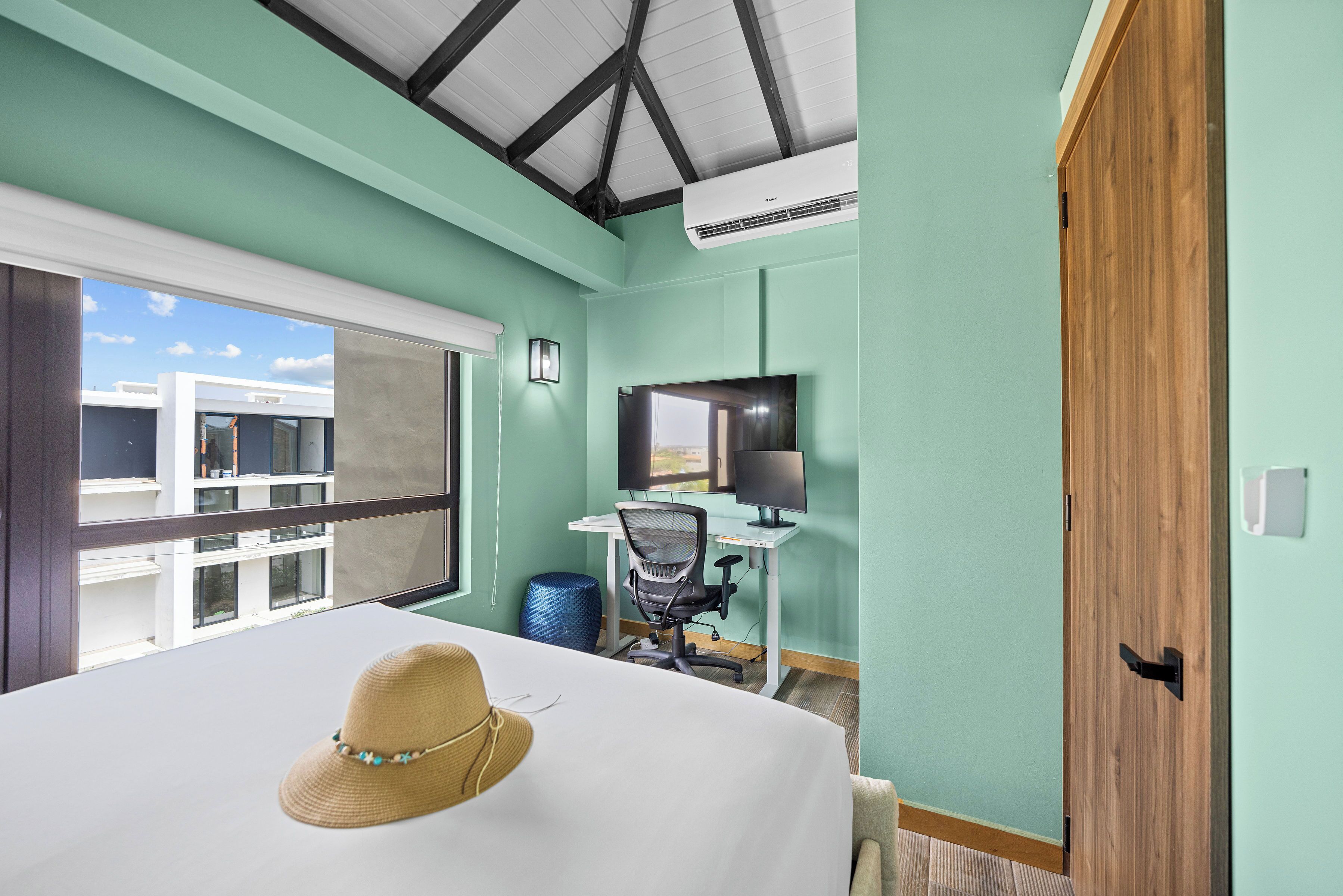 Camera d'albergo con un letto, una scrivania con un computer, una TV e vista su un edificio.