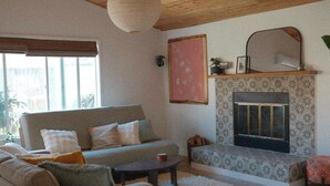 A living room with a sofa, a fireplace, a hanging light fixture, and a window. - Lilac Home-Cozy home w/hot tub. Walking distance to Autzen, fine dining/shopping (Eugene)