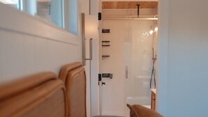 A room with a wooden headboard, a blue sofa, and a door leading to a shower area. - Lilac Home-Cozy home w/hot tub. Walking distance to Autzen, fine dining/shopping (Eugene)