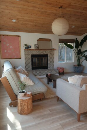 A living room with a fireplace, wooden ceiling, and a large plant.