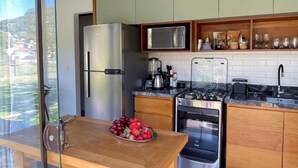 A modern kitchen with wooden cabinets, stainless steel appliances, and a glass door leading to a balcony. - Paraíso na Ferrugem - SC (Garopaba)