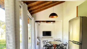 A modern kitchen with a stainless steel refrigerator, a dining area with a round table and chairs, and a wooden ceiling. - Paraíso na Ferrugem - SC (Garopaba)