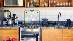 A modern kitchen with wooden cabinets, a built-in microwave, a gas stove, and a stainless steel sink. - Paraíso na Ferrugem - SC (Garopaba)