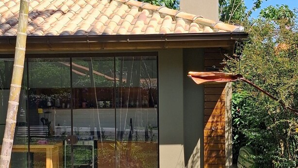 A modern house with a tiled roof, large glass windows, and a wooden deck. - Paraíso na Ferrugem - SC (Garopaba)