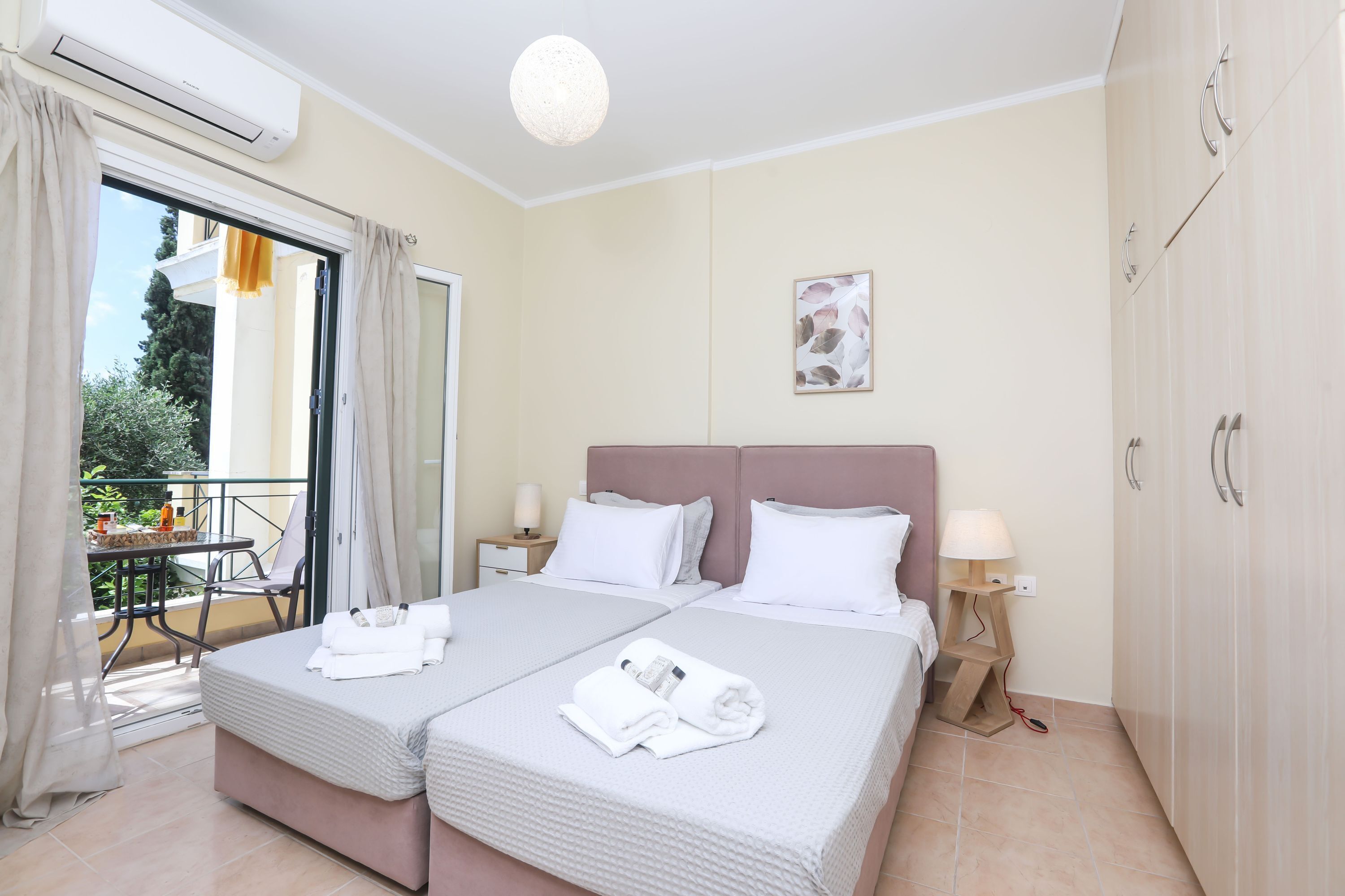 A hotel room with two beds, a balcony, and a view of greenery.