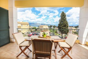 A balcony with two wooden chairs and a table, overlooking a residential area with houses and a mountain in the background.