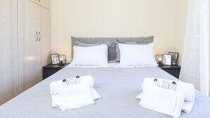 A neatly made bed with white linens and two pillows, a bedside table with a lamp, and a wardrobe with silver handles. - Smart Home Corfu Apartment (Corfu)