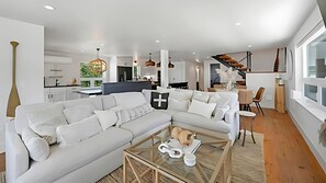 A modern living room with a sectional sofa, a glass coffee table, and a dining area with a staircase.