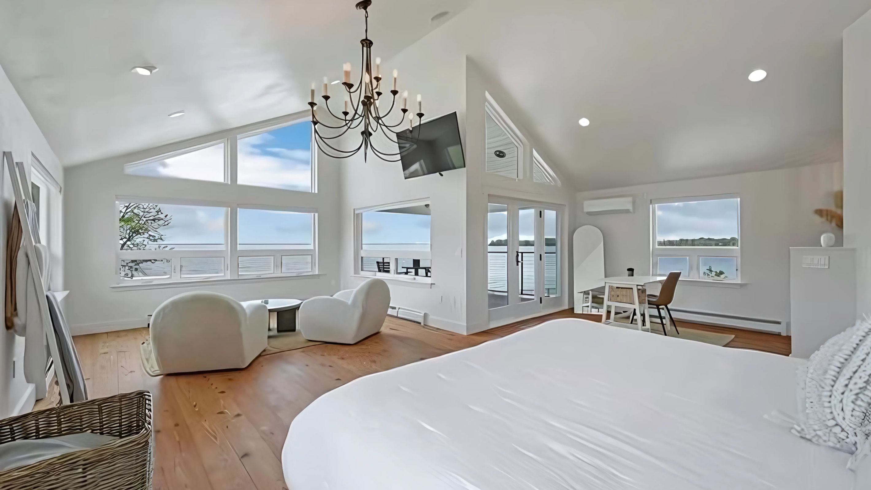 A spacious bedroom with a large bed, a chandelier, and a TV mounted on the wall.