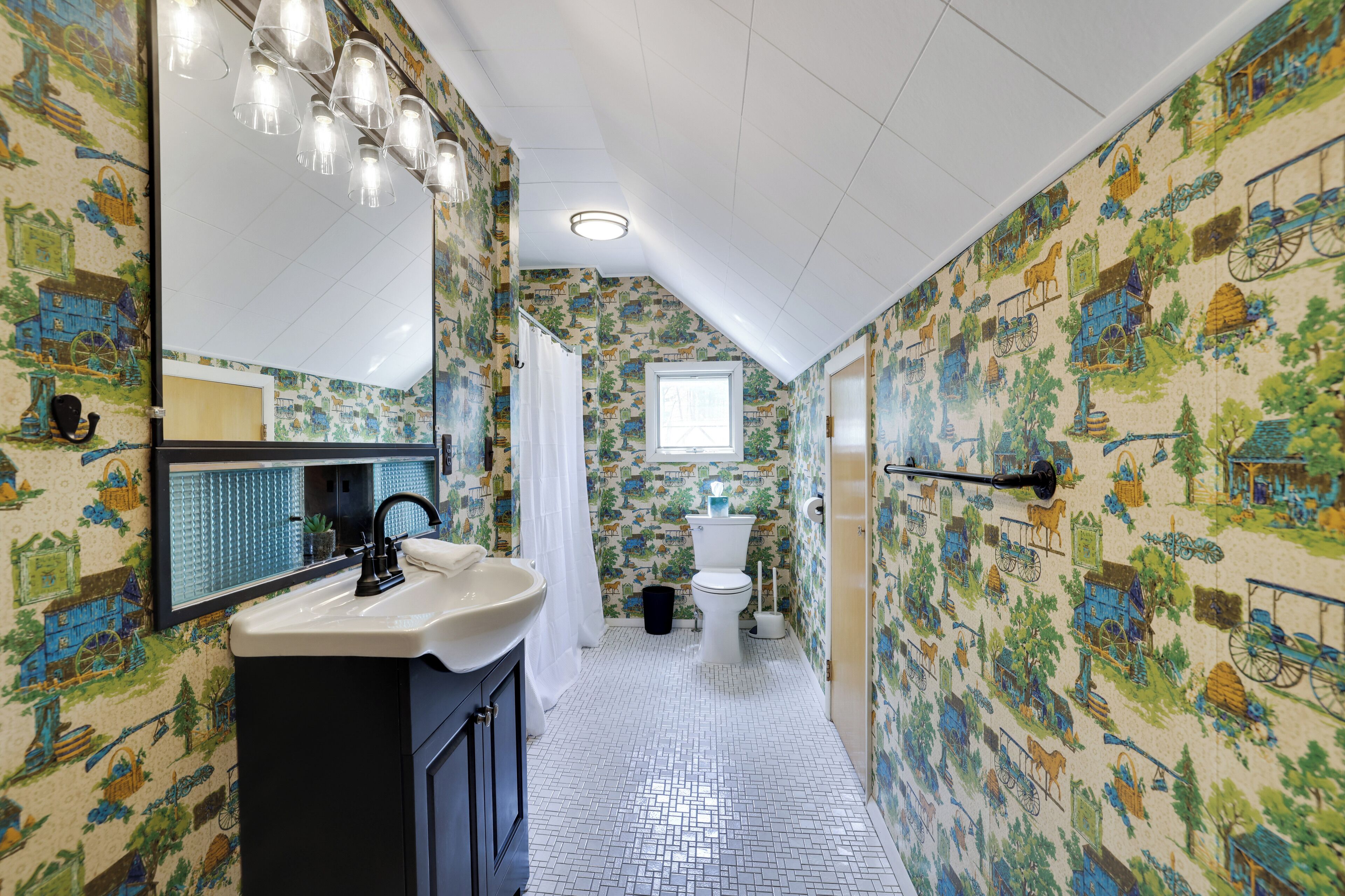 A bathroom with a sink, mirror, and toilet, featuring patterned wallpaper and a tiled floor.