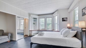 Une chambre avec un grand lit, un canapé gris et une fenêtre donnant sur des arbres.