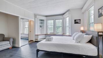 A bedroom with a large bed, a grey sofa, and a window with a view of trees.
