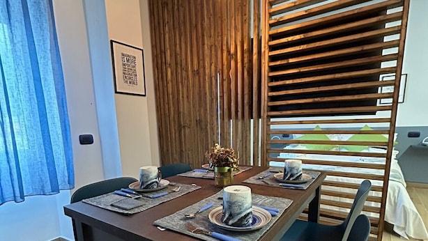 Un coin repas avec une table en bois dressée pour quatre personnes, un luminaire suspendu et une vue à travers une cloison en lattes de bois.