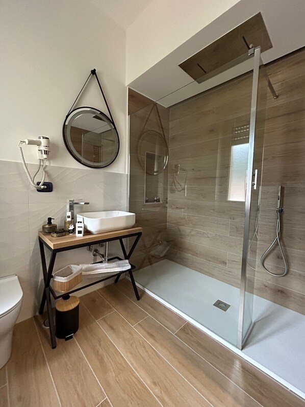 Un baño moderno con ducha de vidrio, espejo redondo y tocador de madera.