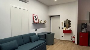 Un salon moderne avec un canapé vert foncé, un petit coin cuisine doté d’un réfrigérateur rouge et une porte blanche.