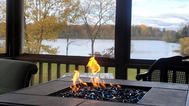 A covered outdoor area with a fire feature and a view of a lake and trees.